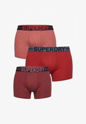 Trois boxers rouges pour homme dans différentes nuances, chacun avec une ceinture noire affichant le nom de la marque « SUPERDRY » en lettres grasses.