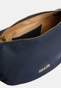 Borsetta in tessuto blu navy con apertura zip, caratterizzata da una cerniera dorata e dettagli con logo. L'interno è in tessuto beige con un piccolo scomparto con zip.