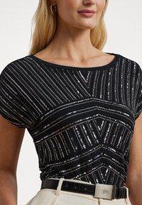 Černá flitrová blůza s geometrickým vzorem, krátkými rukávy a kulatým výstřihem, doplněná texturovaným černým pásem.