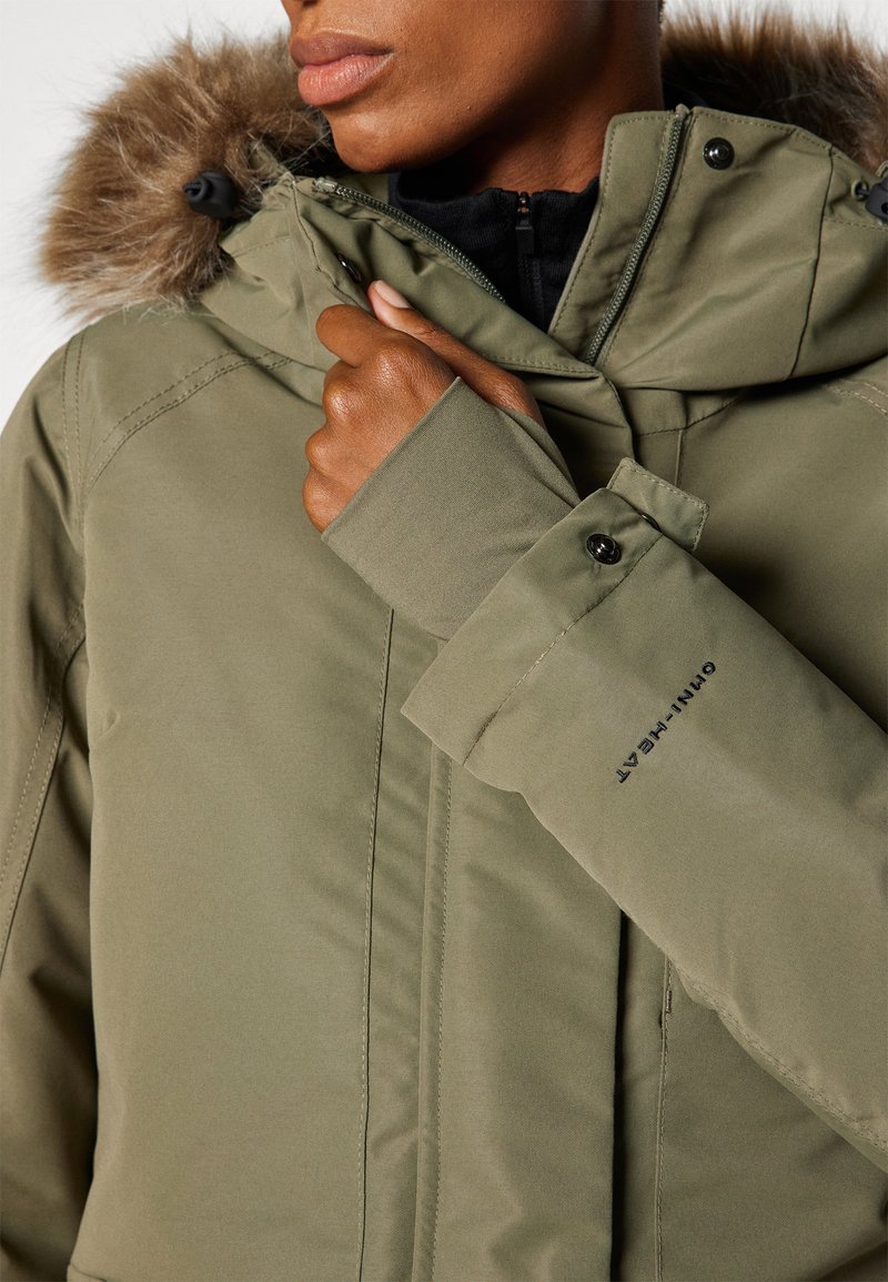 Olivgrüner Parka mit Kapuze aus Kunstfell, Reißverschluss und Druckknopfverschlüssen, Details an den Ärmeln und "OMNI-HEAT" Branding auf dem Ärmel.