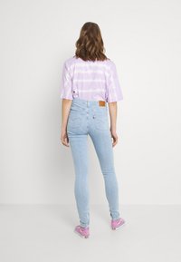 Violetit värjäyksellä t-paita, joka on yhdistetty vaaleansinisiin slim fit -farkkuihin. Huomionarvoisina yksityiskohtina ovat ruskea nahkapatchi farkkujen takaruusukkeessa.