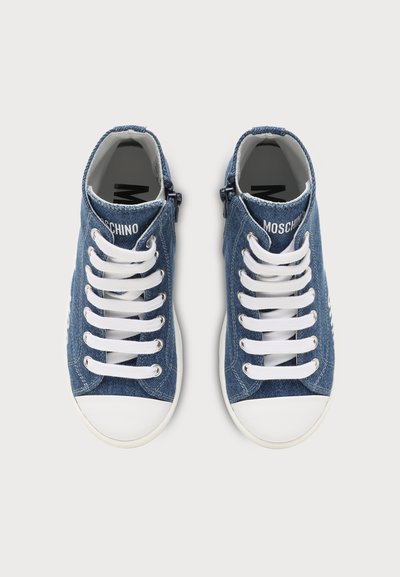 Paire de baskets montantes en denim bleu avec bouts en caoutchouc blanc, lacets blancs, fermetures éclair latérales et marque "Moschino" sur la languette.