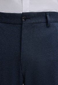 Granatowe spodnie wykonane z teksturowanej tkaniny, z zapięciem na guzik, płaskim przodem oraz szlufkami na pasek.