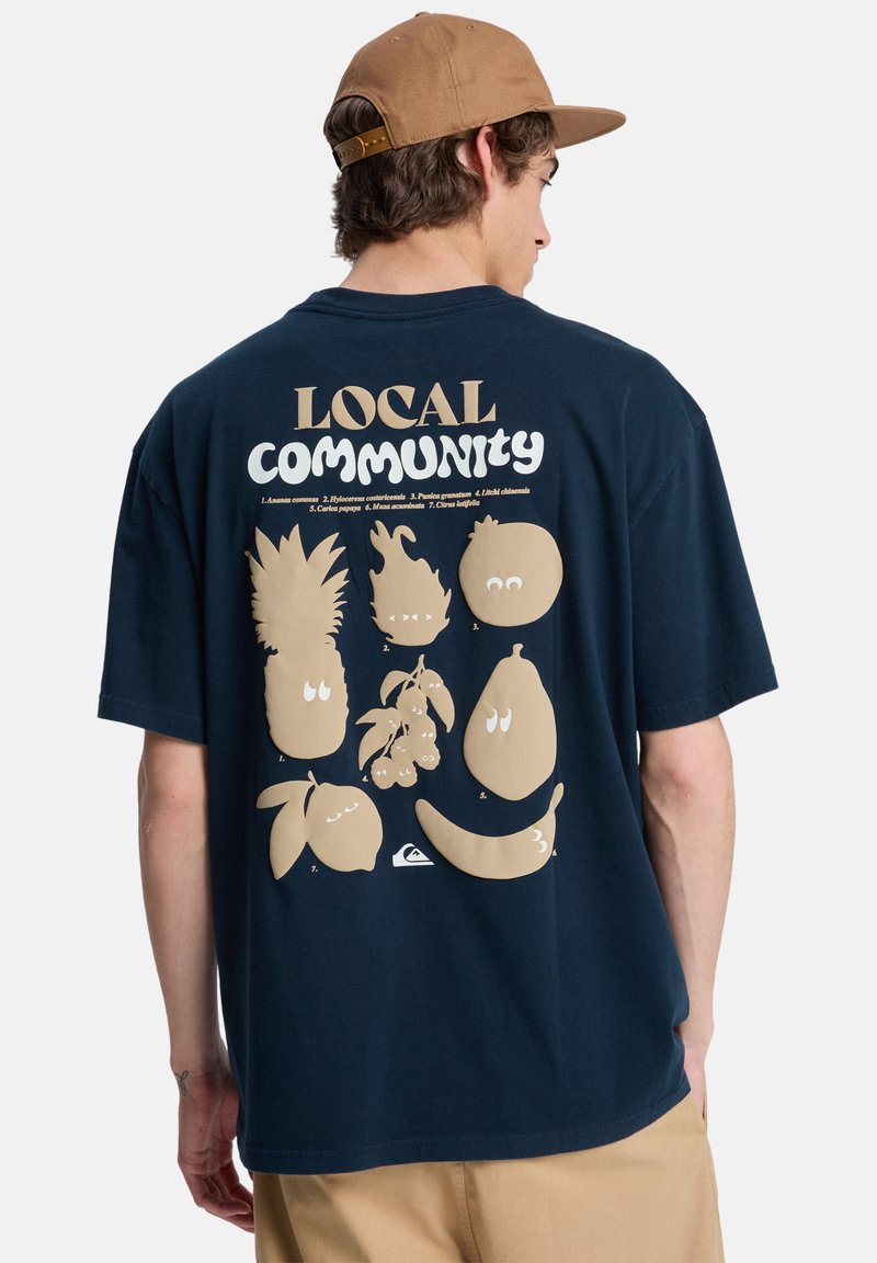 Μπλε βαμβακερό t-shirt με σχέδιο στην πλάτη που απεικονίζει παιχνιδιάρικα φρούτα σε μπεζ, το κείμενο «LOCAL COMMUNITY» και το λογότυπο Quiksilver.