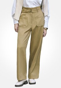 Spodnie cargo w jasnobrązowym bawełnianym materiale, z wysokim stanie, szerokimi nogawkami, dwiema przednimi kieszeniami oraz dopasowanym paskiem z okrągłą klamrą.