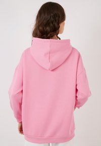 Felpa rosa con una texture morbida e liscia, caratterizzata da un ampio cappuccio, spalle scese e polsini e fondo a costine.