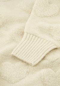 Crème-kleurige trui met getextureerde hartpatronen, geribbelde manchetten en een zachte, donzige stof. Warme, uitnodigende textuur en een gezellige uitstraling.