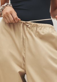 Pantaloni beige chiaro con vita elastica, cordoncino regolabile e tessuto morbido. Presentano tasche laterali e una vestibilità comoda.