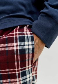 Haut à manches longues bleu marine associé à un pantalon de pyjama à carreaux rouge, bleu marine et blanc, avec une texture douce et une poche latérale.