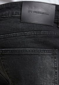 Jeans de mezclilla negros con una textura suave, ligero brillo y una etiqueta de cuero que muestra "ZY PREMIUM" en la cinturilla.