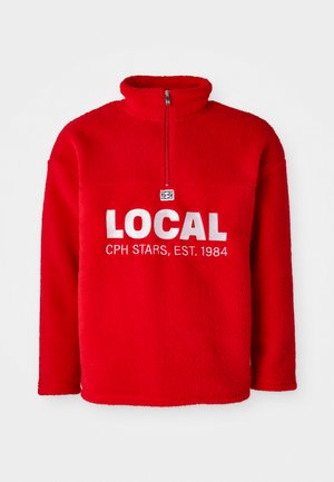 Röd fleece-tröja med hög krage, halv dragkedja framtill och vit broderad text "LOCAL CPH STARS, EST. 1984" på bröstet.