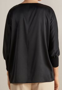 Blusa in satin nero con vestibilità ampia, caratterizzata da un collo rotondo e maniche lunghe a sbuffo. Texture liscia e design pulito e minimale.