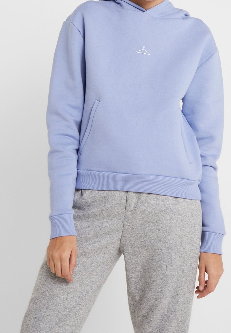 Sudadera ligera de color púrpura hecha de tela suave, con un bolsillo frontal, puños acanalados y un pequeño logo de perchita blanca. Combinada con pantalones de chándal grises.