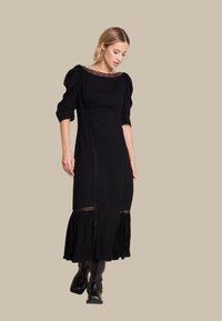 Svart langermet kjole med en tettsittende bodice, samlet pufferm, blondekant rundt halsen og en lagdelt skjørt. Båret med svarte støvler.