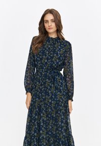 Navy blue long-sleeved dress with floral pattern in green and light blue. Features a gathered neckline and a tie at the waist. Sheer fabric.