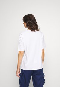 Camiseta blanca de algodón con mangas cortas y escote redondo, que presenta un corte relajado y una textura suave, vista desde la parte de atrás.