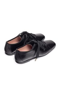 Le scarpe in pelle nera presentano una punta quadrata, una suola piatta e lacci neri in raso. L'interno è di un rosa chiaro, con un marchio discreto sul tallone.