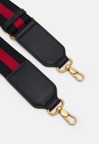 Cinghia regolabile nera con strisce rosse, connettori in pelle e hardware in metallo dorato. Texture liscia con costruzione robusta.