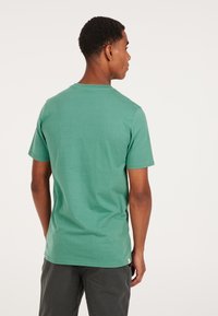Grøn bomulds t-shirt med korte ærmer, rund hals og glat tekstur, vist fra ryggen mod en hvid baggrund.