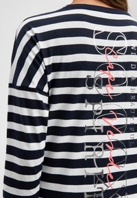 Navy and white striped long-sleeve shirt featuring metallic text on the back, with a slightly loose fit and soft fabric texture.