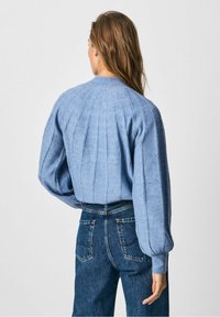 Jasnoniebieski sweter z dzianiny o prążkowanej strukturze i bufiastej rękawach, noszony z dżinsami o wysokim stanie. Szczegóły pionowych szwów z tyłu.