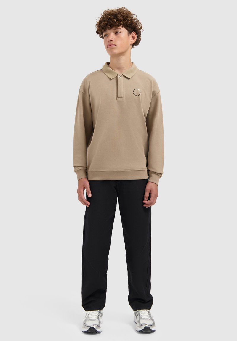 Beige poloshirt met lange mouwen, een kraag en geborduurde details, gecombineerd met zwarte broek en zilveren sneakers. Glad textuur van de stof.