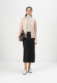 Light pink knitted cardigan with round neckline, gray striped turtleneck, black satin skirt, and gray slip-on shoes. Sleek, modern look.