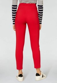 Leggings rouges taille haute avec une texture lisse et une coupe fuselée. Comprend deux poches arrière, associés à des baskets blanches avec des accents noirs.