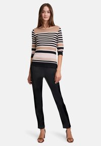 Gestreiftes Langarmoberteil in Beige, Schwarz und Creme mit einem Bootsausschnitt; kombiniert mit enganliegenden schwarzen Hosen und braunen Absatzsandalen.