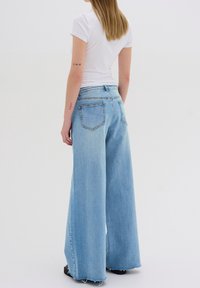 Vaqueros de pierna ancha de cintura alta, en un tono azul claro, con un dobladillo sin acabar, diseño de cinco bolsillos y costuras en contraste. La tela parece suave y con apariencia de denim.