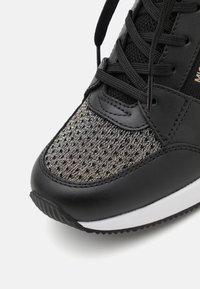 Schwarze Sneaker mit einem Mesh-Obermaterial und silberner Fadenführung, schwarzen Lederakzenten, einer kontrastierenden weißen Sohle und schwarzen Schnürsenkeln.