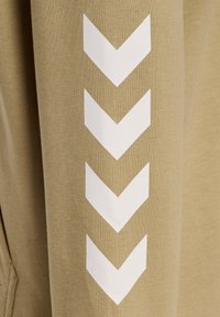 Khaki sweter z rękawami, na których widnieją trzy białe wzory chevronu biegnące pionowo. Materiał jest fakturowany, z jednolitą tkaniną.