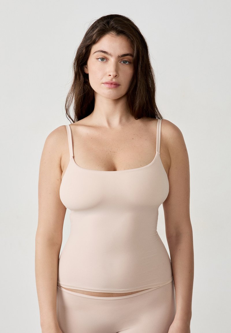 Nude-colored tank top made of stretchy, smooth fabric with thin straps and a square neckline, designed for a fitted silhouette.