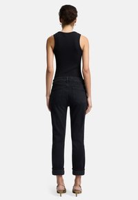 Schwarzes, geripptes Tanktop kombiniert mit schwarzen Denim-Jeans. Die Jeans haben ein gerades Bein, aufgerollte Säume und zwei Gesäßtaschen.