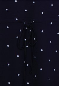 Tecido azul-marinho com bolinhas brancas, apresentando um cordão na cintura. Textura suave e distribuição uniforme do padrão.