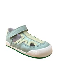 Un zapato sintético azul claro con recortes de malla, correa de Velcro, suela blanca y acento verde en la parte inferior. Presenta un diseño aerodinámico.