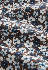 Baumwollstoff mit braunem Hintergrund, verziert mit einem floralen Muster aus weißen und blauen Blumen sowie dunklen grünen Blättern, texturiert und drapiert.