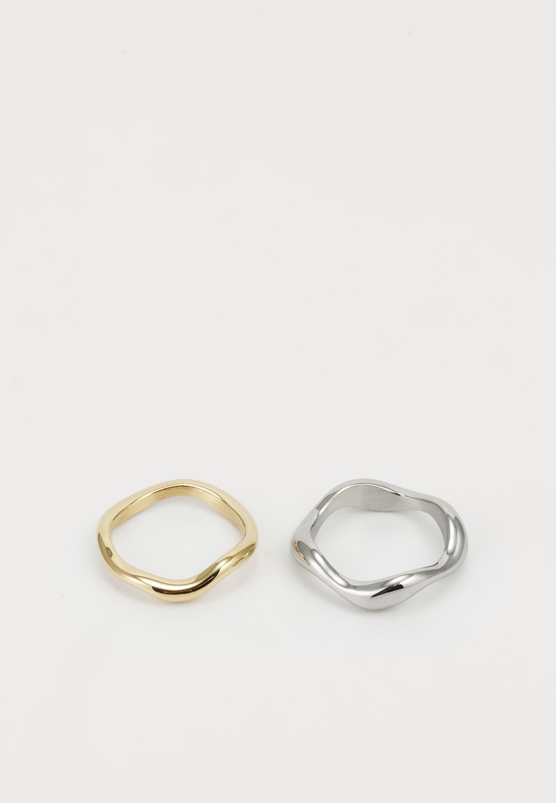 Se muestran dos anillos: uno de oro con un diseño liso y retorcido y uno de plata con una forma retorcida similar, ambos sobre un fondo blanco.