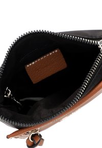 Interno in tessuto nero di una borsa con un accento in pelle marrone. Presenta una chiusura con cerniera e un piccolo tag rettangolare in pelle all'interno.