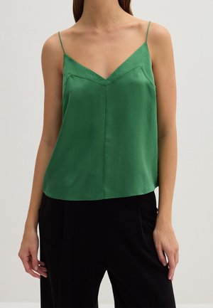 Grünes Satin-Camisole mit dünnen Trägern, V-Ausschnitt, taillierter Passform und glatter Textur, kombiniert mit locker sitzenden schwarzen Hosen.