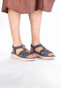 Blauwe strappy sandalen met decoratieve hardware, een gevoerde witte zool en een open teen ontwerp, geschikt voor casual gebruik.