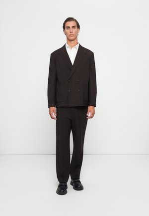 Dark brown double-breasted suit with a structured design, featuring a notched lapel, two front pockets, paired with a white shirt and black shoes.