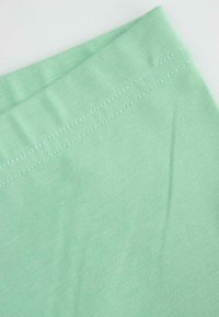 Miętowa tkanina o gładkiej strukturze, z płaskim paskiem w talii i kontrastowym białym przeszyciem wzdłuż krawędzi.