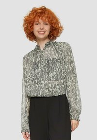 Transparante blouse met een abstract zwart-wit patroon, voorzien van een gathering in de hals en knoopdetails, gecombineerd met zwarte broek.