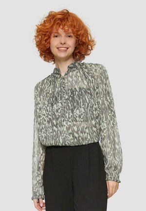 Transparante blouse met een abstract zwart-wit patroon, voorzien van een gathering in de hals en knoopdetails, gecombineerd met zwarte broek.