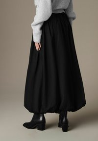 Falda nera fluente con vita arricciata e orlo arrotondato, abbinata a stivali neri aderenti alla caviglia e un maglione lavorato a maglia grigio chiaro.