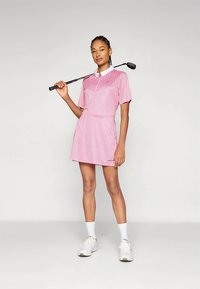 Vestido de golf con mangas cortas, rayas verticales rosas y blancas, cuello, diseño entallado y acampanado, combinado con zapatillas blancas y un palo de golf.