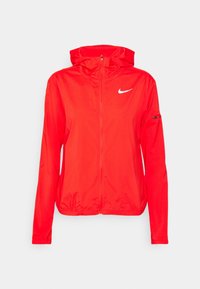 Červená bunda Nike se zipem vpředu, kapucí, elastickými manžetami a pasem. Obsahuje bílé logo na levé straně hrudi a zipovou kapsu na paži.
