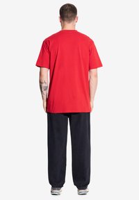 Czerwona bawełniana koszulka z luźnym krojem, krótkimi rękawami i prostym dołem, zestawiona z luźnymi, ciemnoniebieskimi dżinsami.