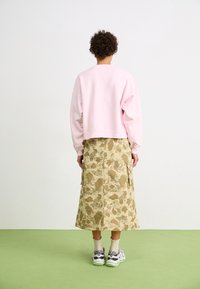 Lichtroze cropped sweatshirt, midirok in camouflagepatroon in beige tinten, witte sneakers met grijze accenten en groene zolen.